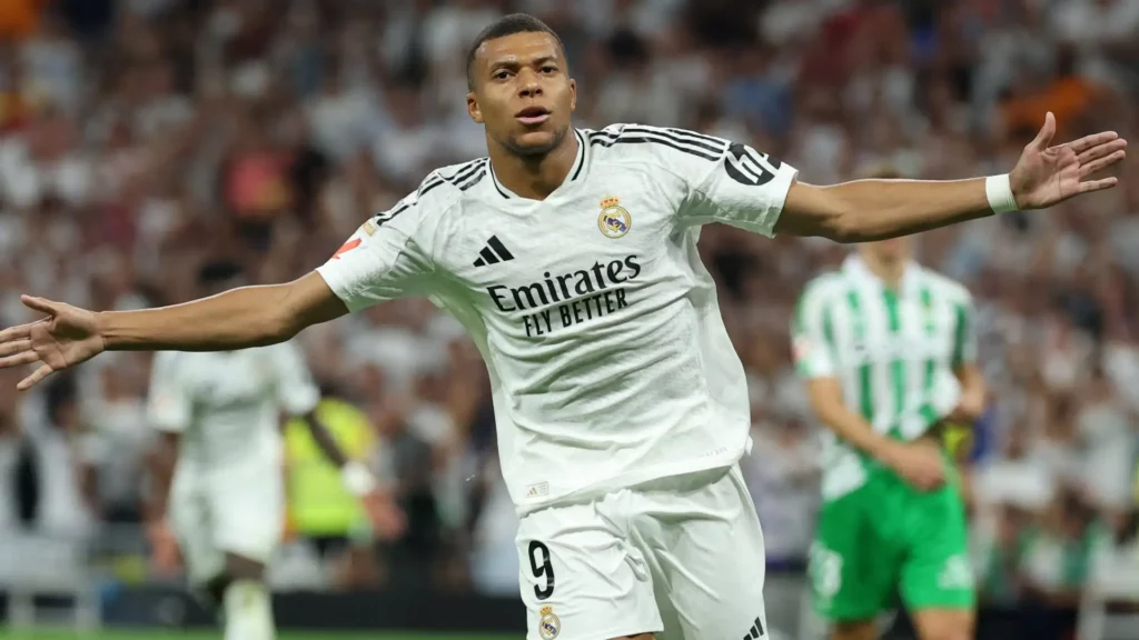 Kylian Mbappé slaví svůj gól v dresu Realu Madrid při zápase proti Realu Betis, s roztaženými pažemi, na stadionu plném fanoušků.