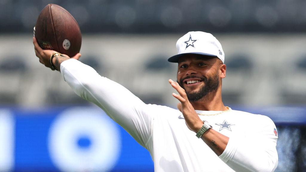 Dak Prescott, quarterback Dallas Cowboys, s úsměvem při tréninku, drží míč v ruce a připravuje se na hod, během předsezónního tréninku NFL.