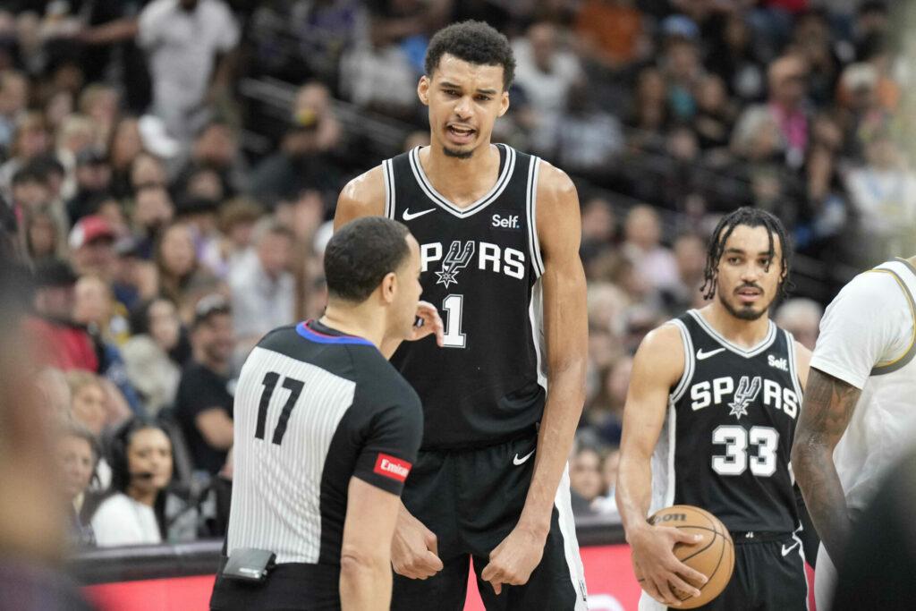 Victor Wembanyama z San Antonio Spurs v diskusi s rozhodčím během přípravného zápasu NBA, s Dresem v pozadí