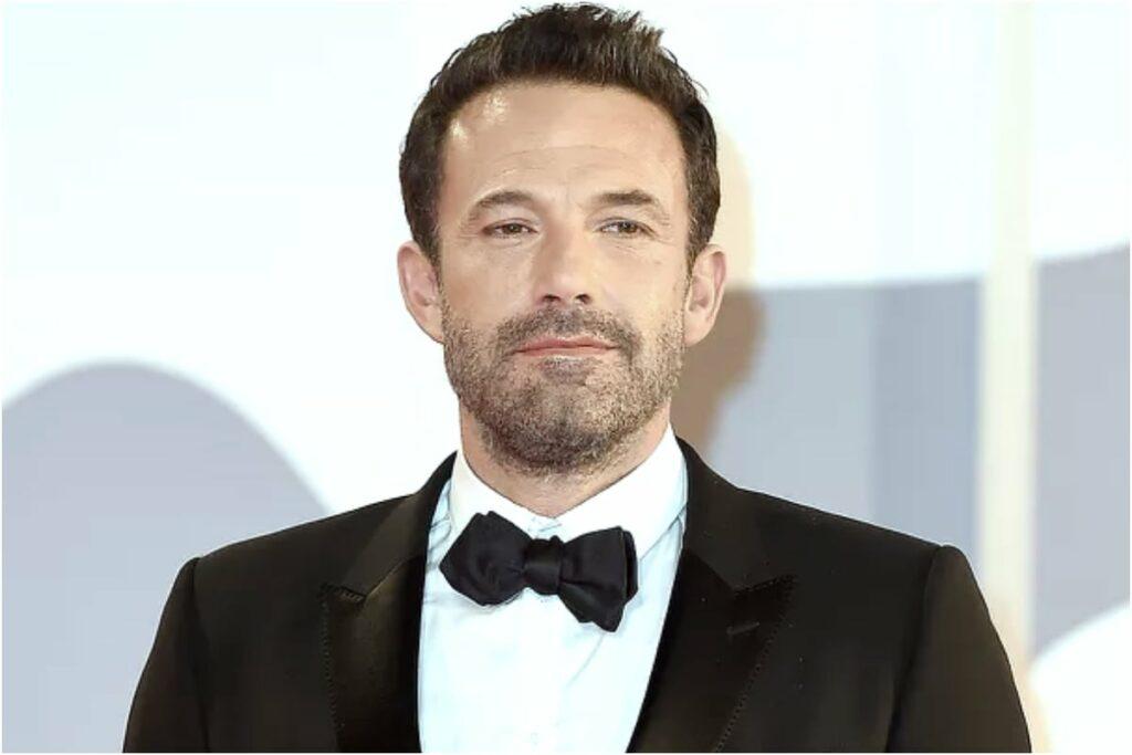 herec Ben Affleck v elegantním obleku pózuje na červeném koberci, známý pro svou hereckou kariéru i vášeň pro blackjack.